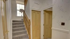 A carpeted staircase with wooden balusters, a light switch, and a door with a floral wallpaper pattern. - The Clachan Wick in Wick (Wick)