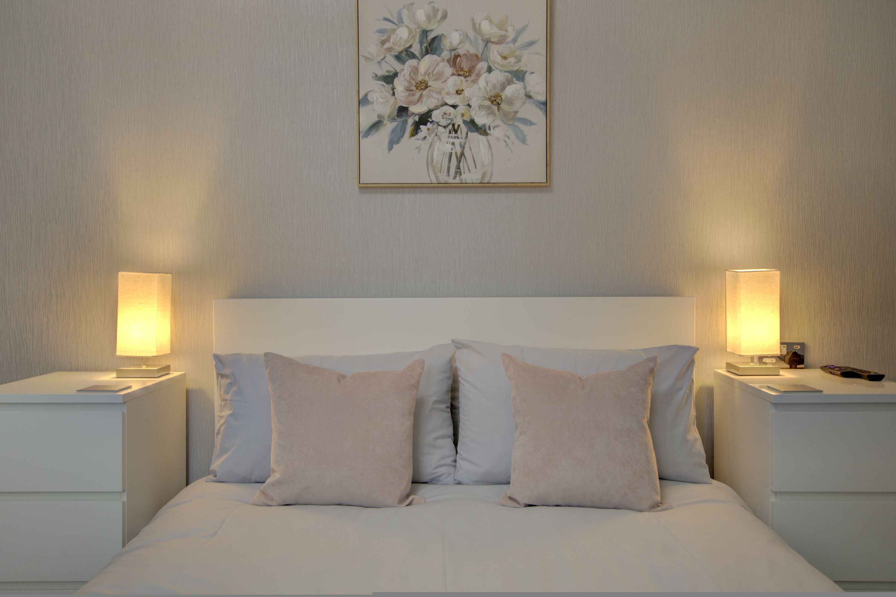 A bedroom with a bed, two bedside tables, and a wall-mounted painting.