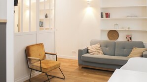 Ein modernes Wohnzimmer mit Holzboden, einem grauen Sofa, einem gelben Sessel und einem weißen Bücherregal.