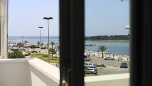A view from a window overlooking a coastal area with parked cars, a road, and a body of water. - Riviera Luxury Rooms (Porto Cesareo)