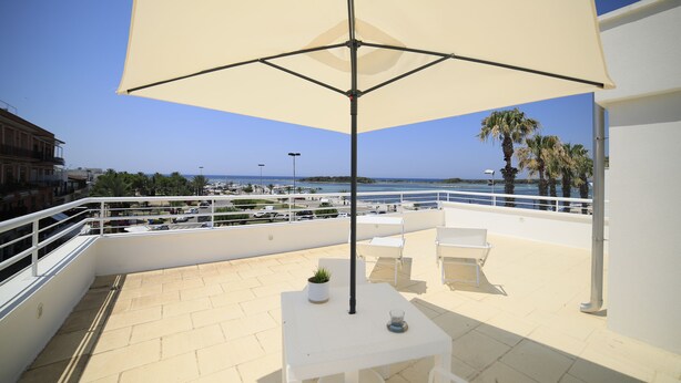 A rooftop terrace with a table, chairs, and a large umbrella. The terrace overlooks a marina and the sea. - Riviera Luxury Rooms (Porto Cesareo)