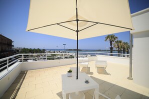 A rooftop terrace with a table, chairs, and a large umbrella. The terrace overlooks a marina and the sea. - Riviera Luxury Rooms (Porto Cesareo)