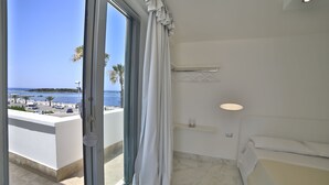 A hotel room with a large sliding glass door leading to a balcony with a view of the sea and boats. - Riviera Luxury Rooms (Porto Cesareo)