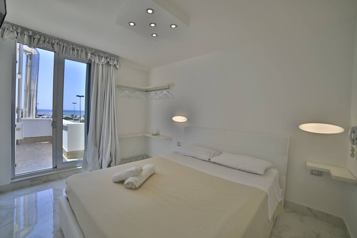 A hotel room with a large bed, a bathroom with a shower, and a view of the sea.
