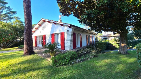 Una casa de dos pisos con fachada roja y blanca, cimientos de piedra y un jardín bien cuidado.