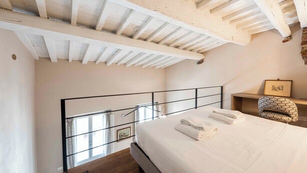 Un dormitorio con techo de madera, cama con ropa de cama blanca, cabecera de metal negro y ventana con cortinas.