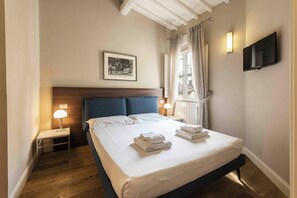 A hotel room with a bed, a nightstand with a lamp, a framed picture on the wall, and a TV mounted on the wall. - Alfani Modern Loft by MMega (Florence)