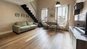 Una sala de estar con sofá, mesa de comedor, sillas, una escalera y televisor.