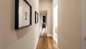 Un pasillo estrecho con suelo de madera, cuadros en las paredes y una puerta al final.