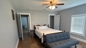 A bedroom with a bed, a blue sofa, a ceiling fan, and a window with blinds.
