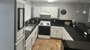 A compact kitchen with white cabinets, a stove, and a sink.