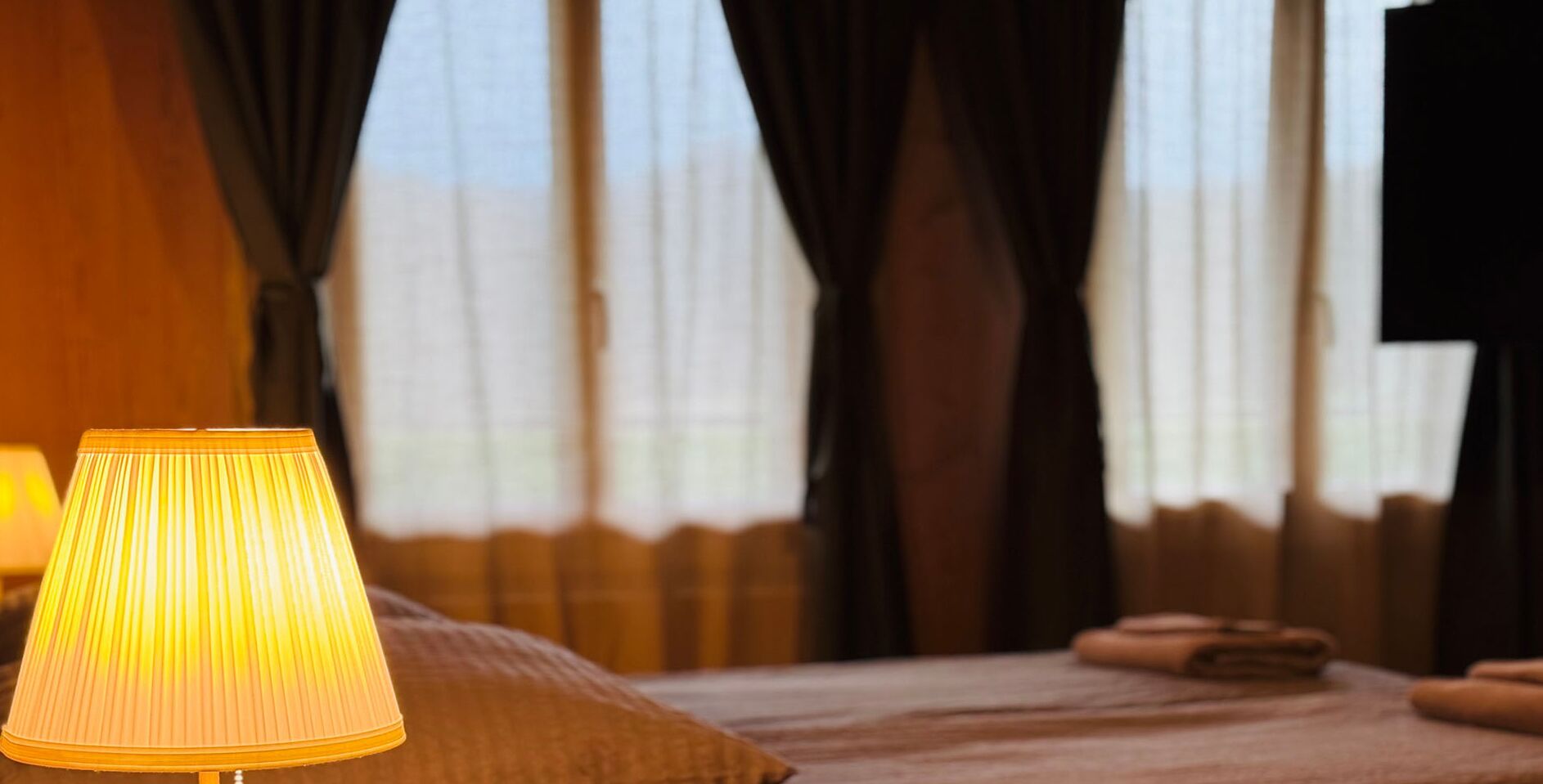 Et hotelværelse med seng, lampe og gardiner.
