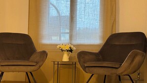 Two armchairs, a small table, and a vase with flowers in a room with a window and curtains.