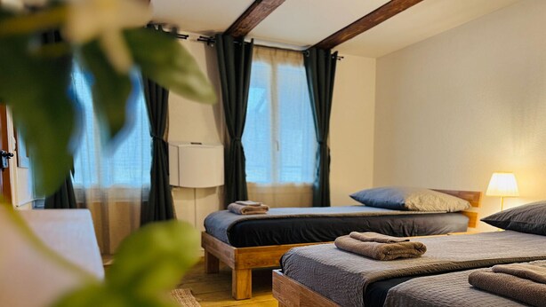 A hotel room with two single beds, a wooden headboard, a bedside lamp, and a window with curtains.