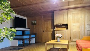 A cozy living room with wooden walls, a TV, a blue cabinet, a small table with a vase of flowers, and a red sofa.