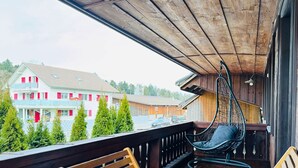 A wooden balcony with a hanging chair and a wooden bench.