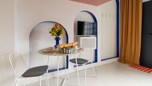 Una camera moderna con un tavolo da pranzo rotondo, due sedie, un vaso con fiori, una televisione a schermo piatto e un'ampia finestra con tende.