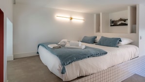Camera da letto moderna con un grande letto, un comodino, una lampada a parete e un quadro con vista sulla città.