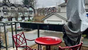 A balcony with a red metal table and chairs, a grey awning, and a view of residential buildings. - Room in townhouse (Vancouver)