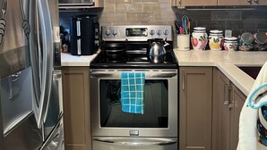 A modern kitchen with stainless steel appliances, wooden cabinets, and a tiled backsplash. - Room in townhouse (Vancouver)