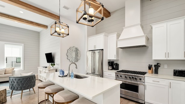 A modern kitchen with white cabinetry, a central island with stools, stainless steel appliances, and pendant lighting.