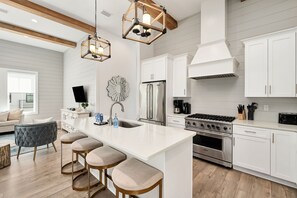 A modern kitchen with white cabinetry, a central island with stools, stainless steel appliances, and pendant lighting.