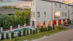A modern two-story residential building with a swimming pool, a covered patio, and a red-lit entrance.