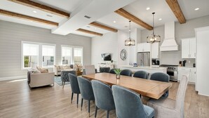 A spacious living area with a wooden dining table, blue chairs, and a kitchen with white cabinets and modern appliances.