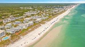 An aerial view of a coastal resort with beachfront properties, a swimming pool, and a beach with umbrellas.