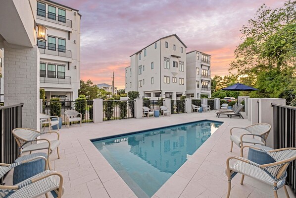 A swimming pool with lounge chairs, a fence, and a building with balconies.