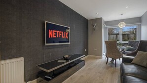 Una sala de estar moderna con un televisor de pantalla plana grande montado en una pared oscura, una mesa de centro de vidrio, un sofá de cuero y una cabeza de venado decorativa en la pared.