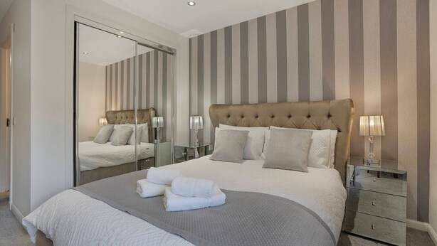 Un dormitorio moderno con una cama grande, un espejo, papel tapiz a rayas y mesitas de noche con lámparas.