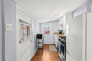 A narrow kitchen with white cabinets, a white refrigerator, and a window with blinds. - Cozy 1-bedroom apartment with WiFi, AC in charming Hazel Park (Hazel Park)