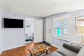 A living room with a flat-screen TV, a gray sofa, a wooden coffee table, and a window with blinds. - Cozy 1-bedroom apartment with WiFi, AC in charming Hazel Park (Hazel Park)