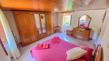 A bedroom with a wooden ceiling, a bed with pink bedding, a dresser, a mirror, and a window.