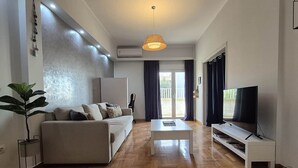 Ein modernes Wohnzimmer mit einer Couch, einem Couchtisch, einem Fernseher und einem großen Fenster mit Vorhängen.
