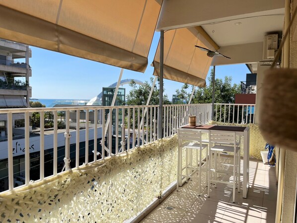 A balcony with a white railing, a table, and a chair. There is a view of the sea and buildings in the background. - Athens Riviera Alimos by Comfort Club, Athens best getaway to enjoy Sea & Culture (Alimos)