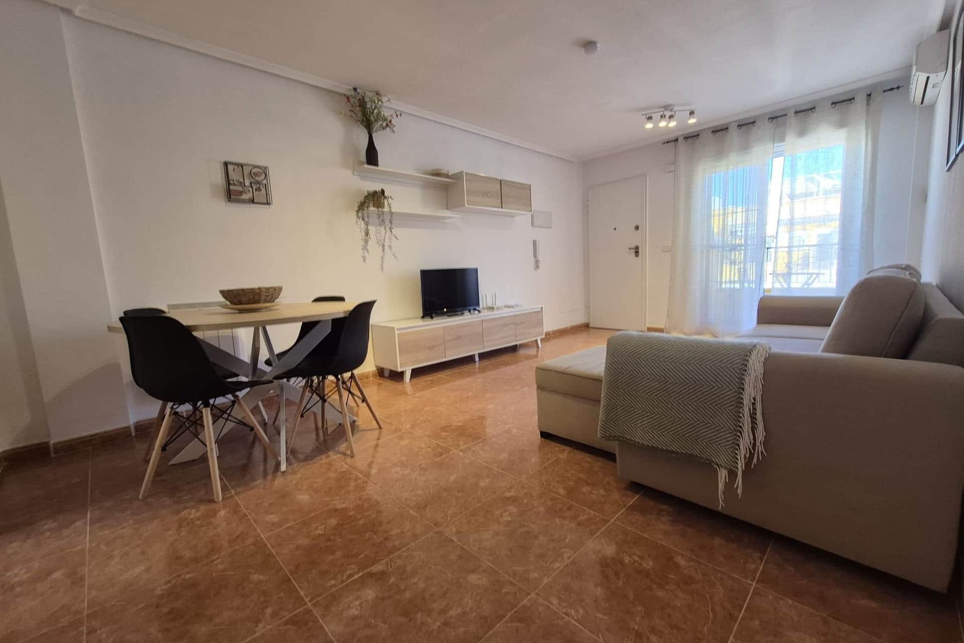 Een woonkamer met een bank, een televisie, een eettafel met stoelen en een plant aan de muur.
