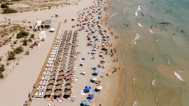 A beach with rows of sun loungers and umbrellas, a lifeguard tower, and a sandy shoreline.