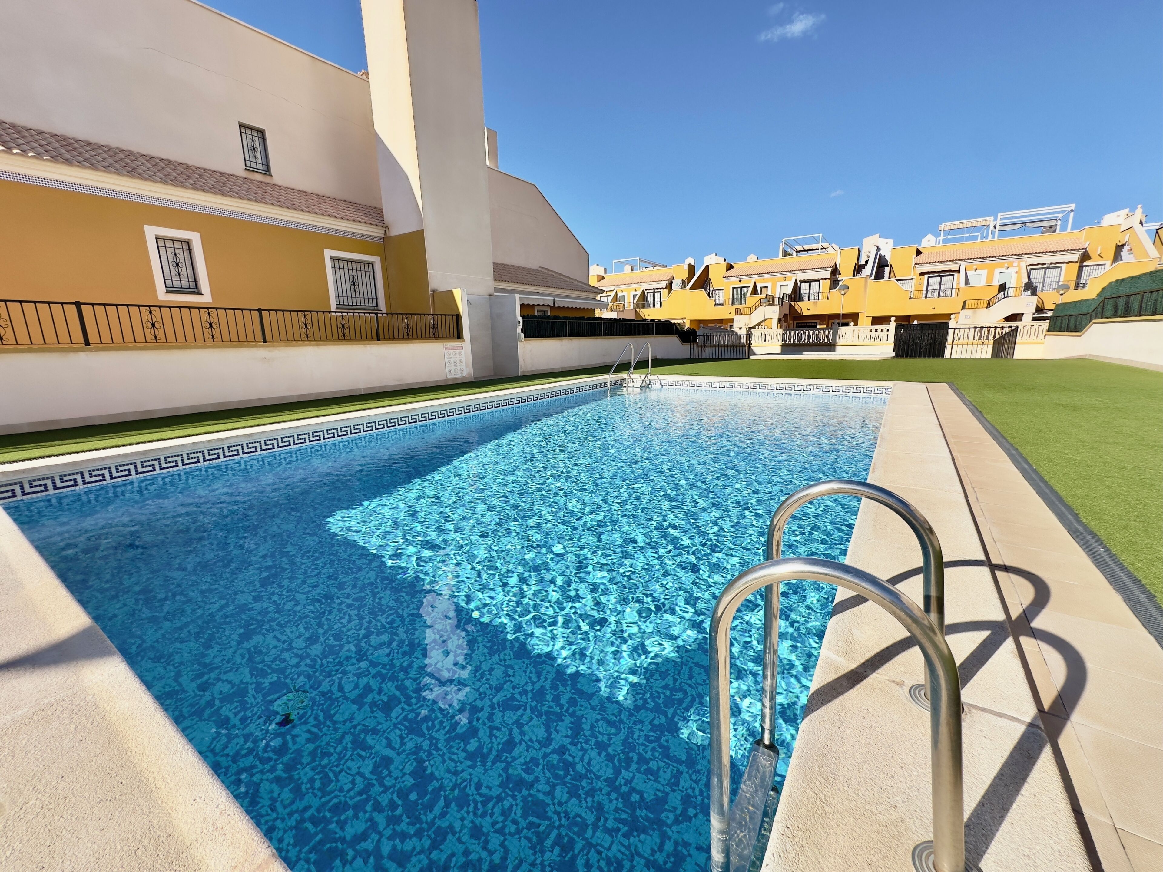 A swimming pool with a clear blue water pattern, surrounded by a concrete deck and a metal ladder.