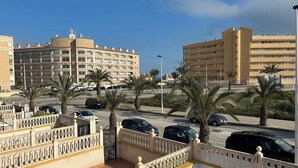 A multi-story hotel with balconies, a parking area with cars, and palm trees.