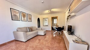 Ein modernes Wohnzimmer mit einem beigefarbenen Ecksofa, einem Essbereich mit rundem Tisch und Stühlen sowie einem Fernseher auf einem weißen Lowboard.