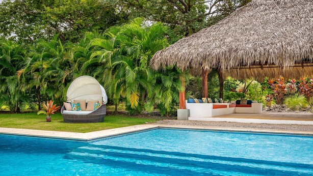 A swimming pool with a thatched-roof structure and a lounge area with cushions. - Spectacular 4BR/4BA Villa with Private Pool & Parking WiFi, AC (Hacienda Pinilla)
