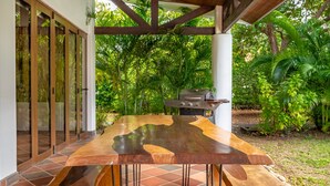 A wooden dining table with benches, a grill, and a view of lush greenery. - Spectacular 4BR/4BA Villa with Private Pool & Parking WiFi, AC (Hacienda Pinilla)