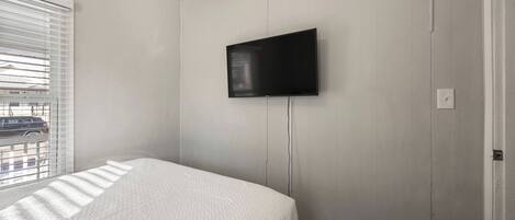 A bedroom with a bed, a television mounted on the wall, and a window with blinds.