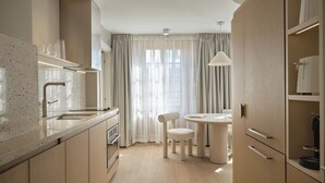A modern kitchen with a central island, a dining area with a round table and chairs, and a large window with sheer curtains. - Corner Apartments  (Montréal)