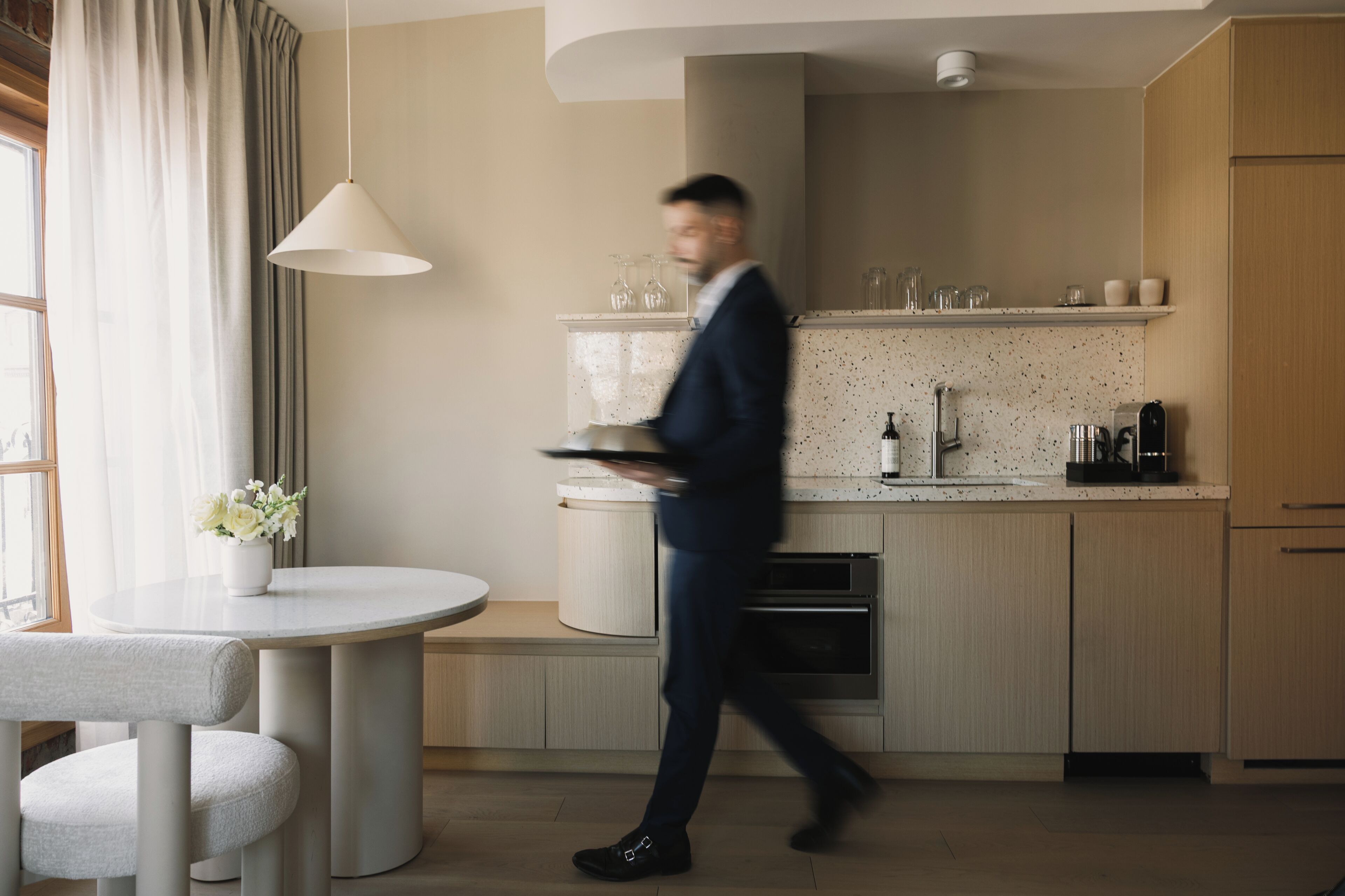 A modern kitchen with a round dining table, a hanging light fixture, and a built-in oven.