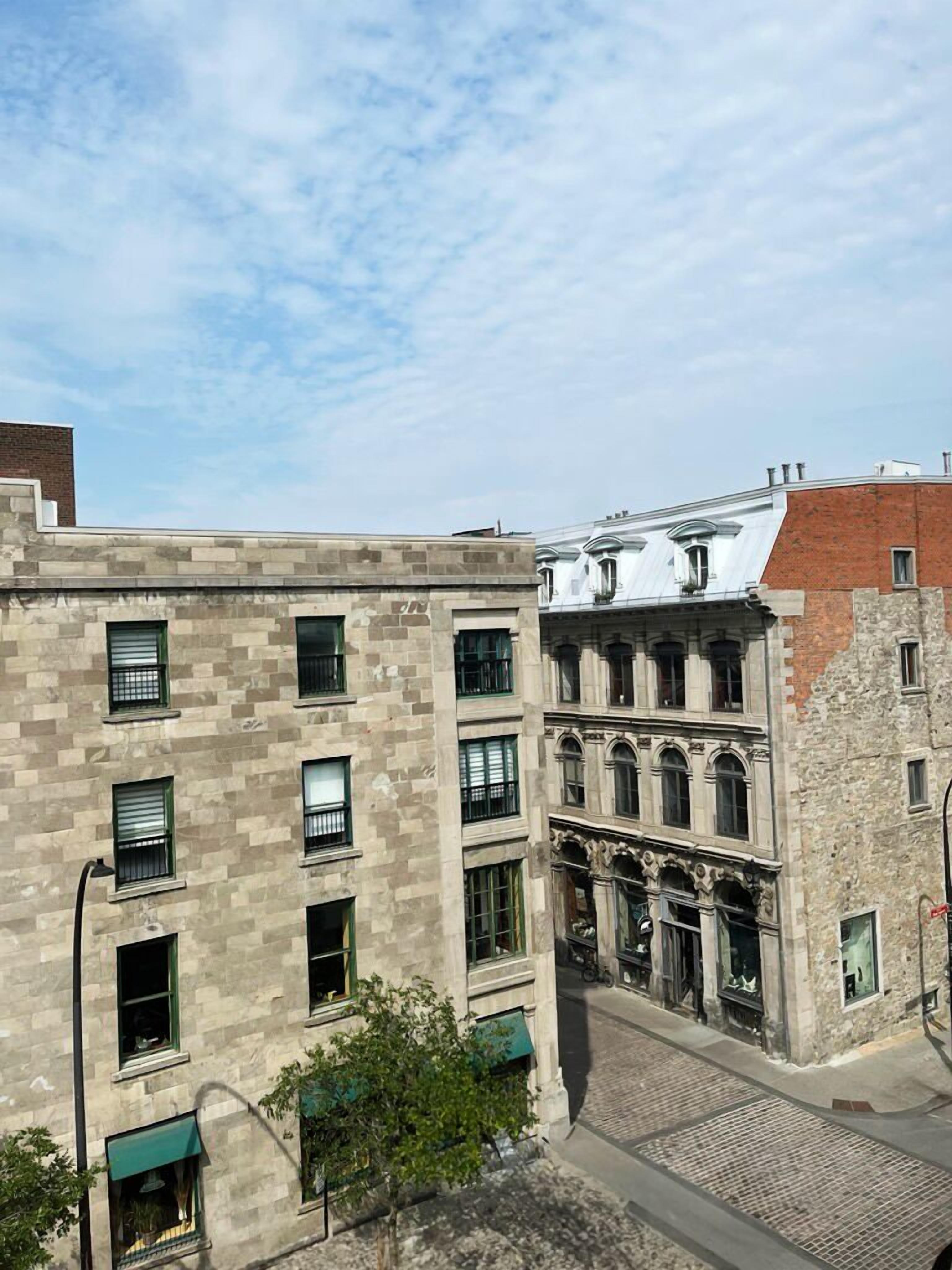 A multi-story building with a stone facade, multiple windows, and a street in front.