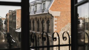 A view through a window with iron bars, featuring a brick building with a sloped roof and large windows. - Corner Apartments  (Montréal)