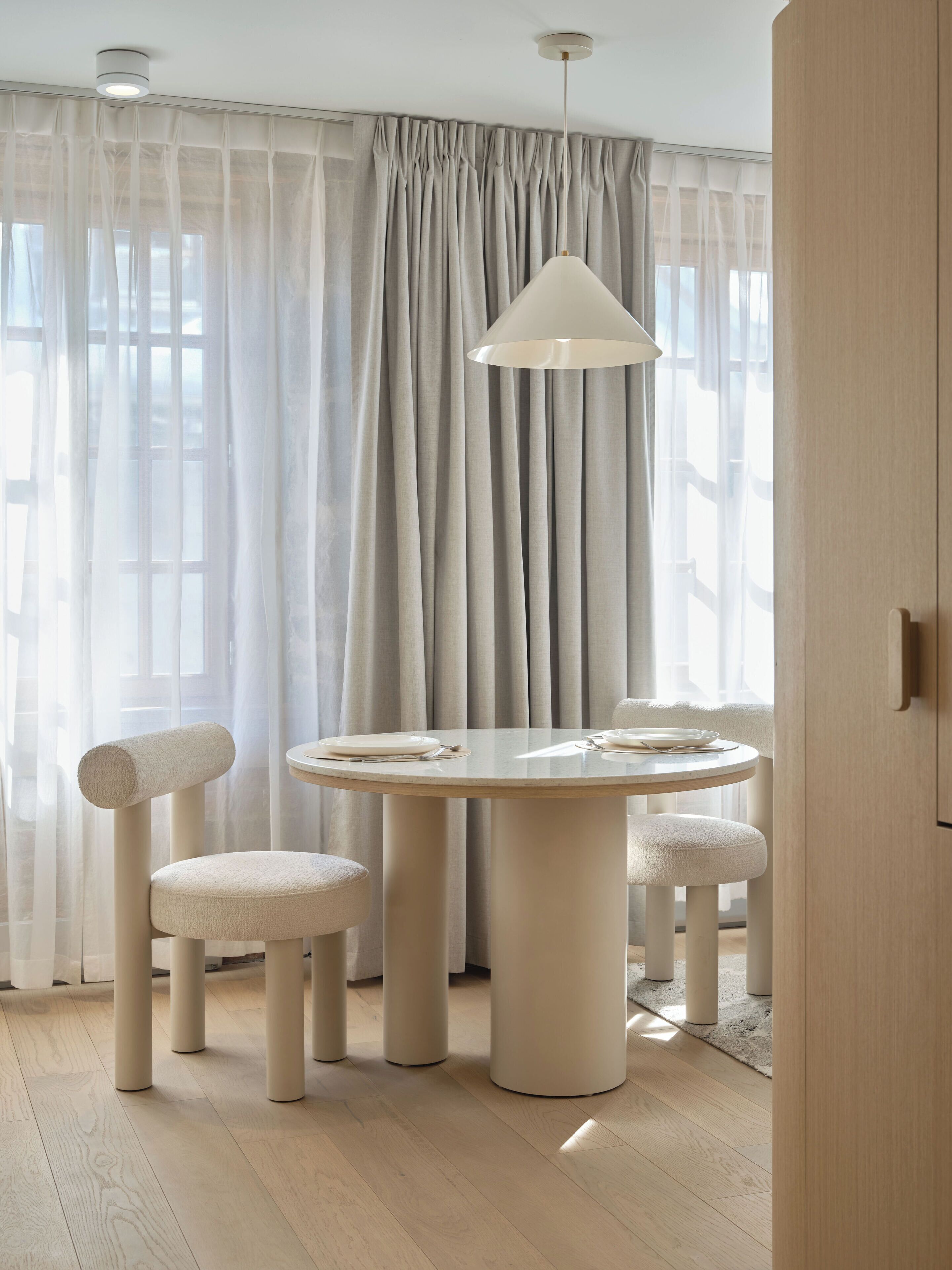 A modern dining area with a round table, four chairs, and a hanging light fixture.